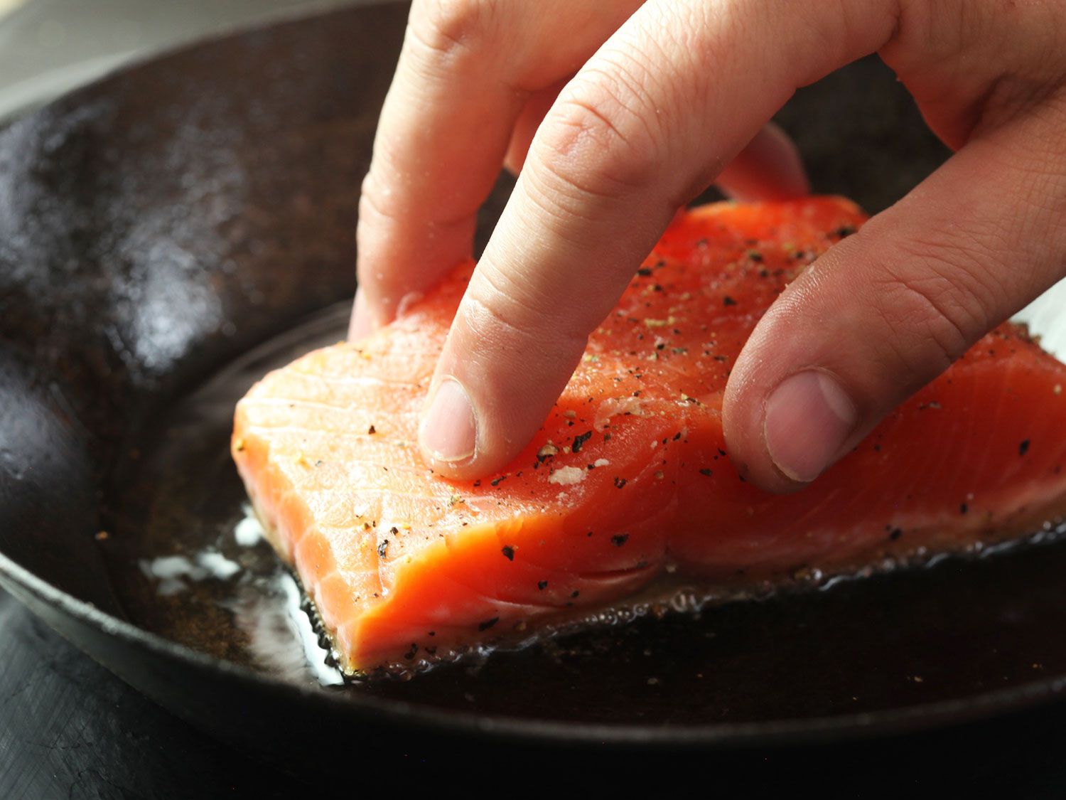 Pressing skin-on salmon fillet into a skillet of hot oil skin-side down.