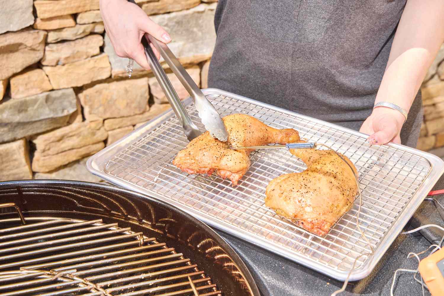 A hand using tongs to move chicken onto a tray from the Weber Performer Deluxe Charcoal Grill 22