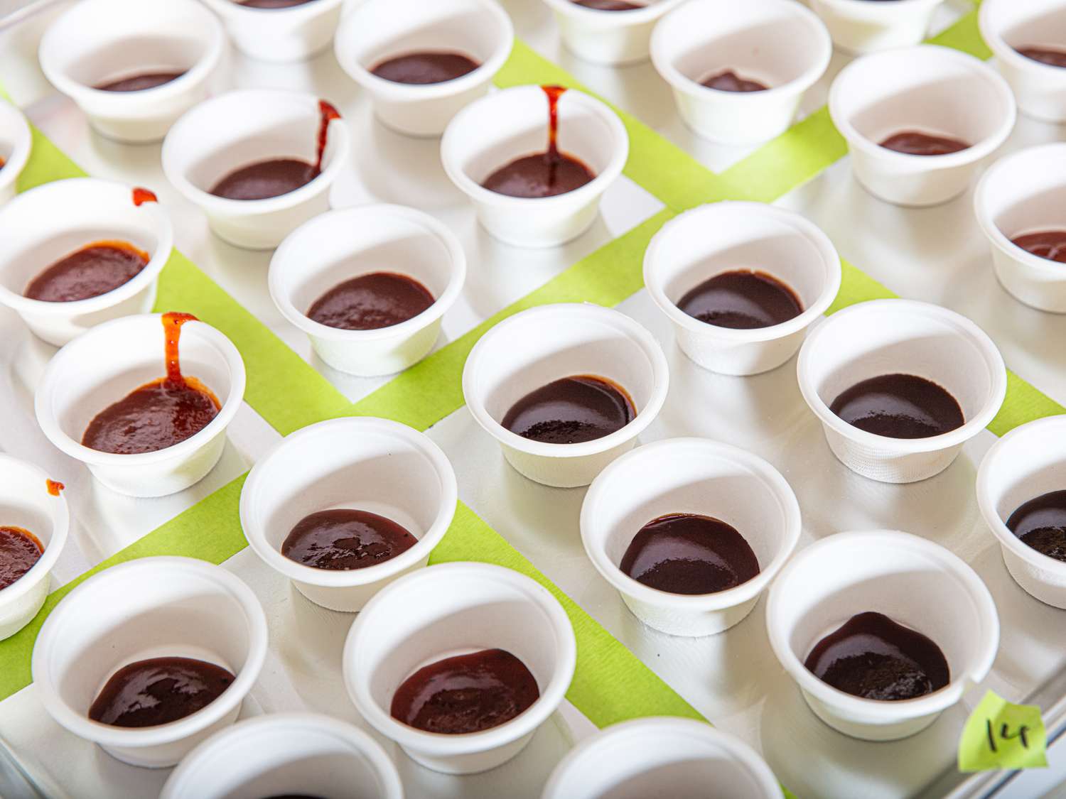 Rows of small condiment cups filled with barbecue sauce on a table
