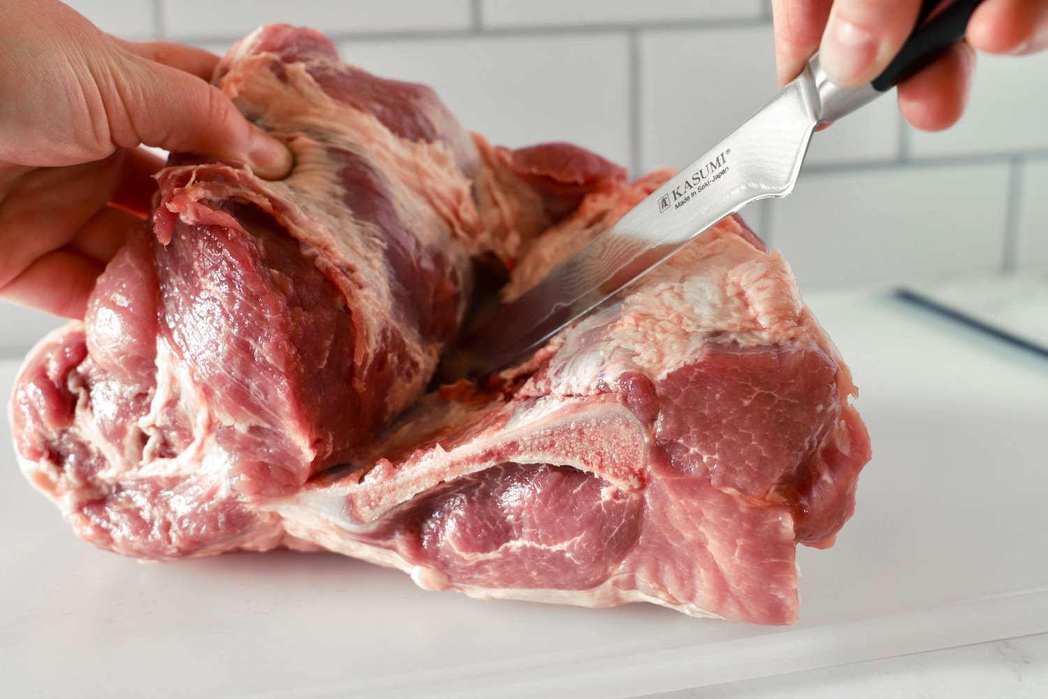 Hands using a boning knife to remove the bone from a pork shoulder