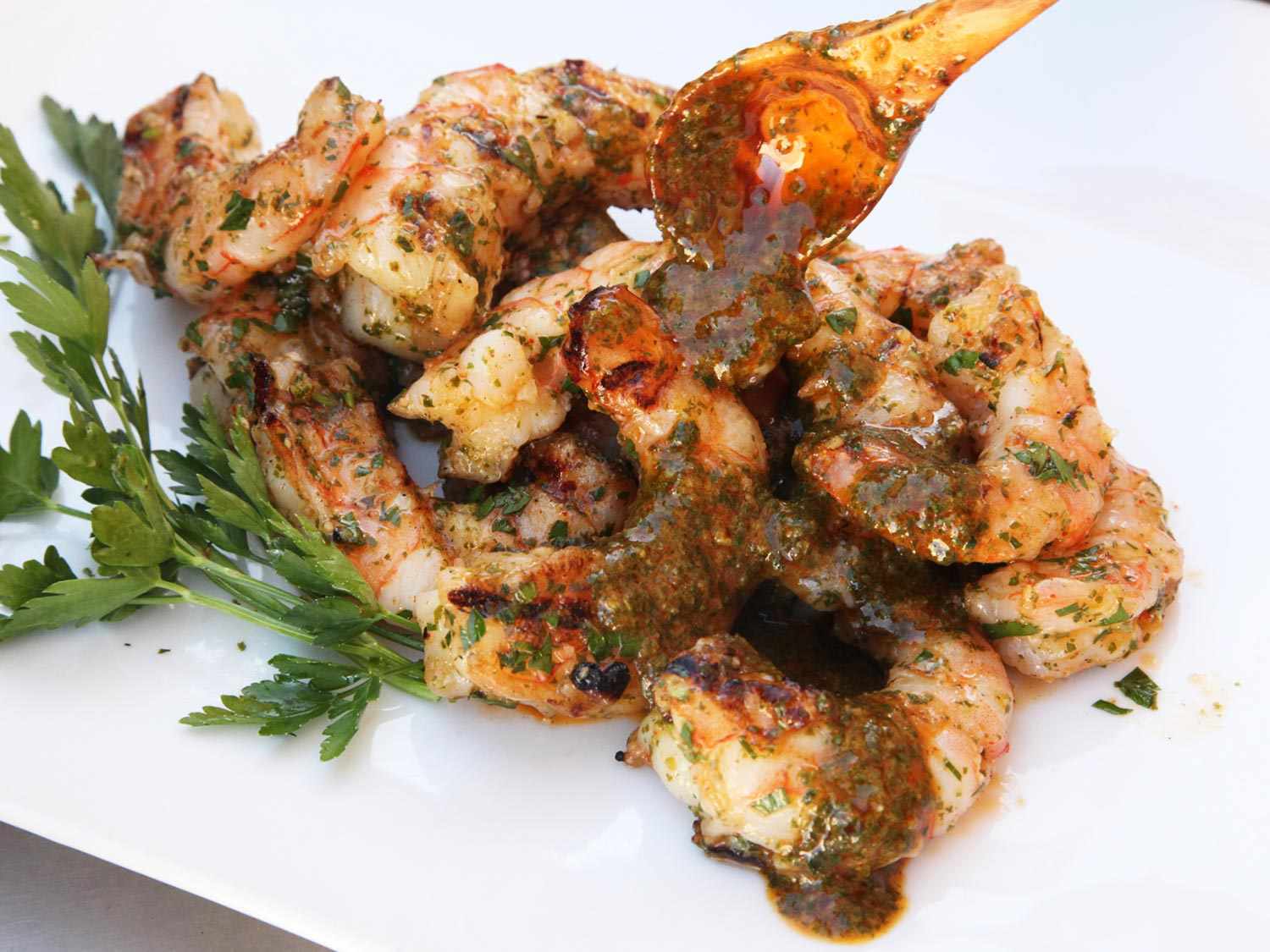 Closeup of chermoula being spooned onto a pile of freshly grilled shrimp.