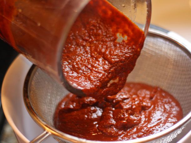 Pouring just blended red chile mixture into a strainer.
