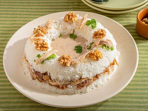 Plated dish featuring layered rice chicken and nuts with garnish