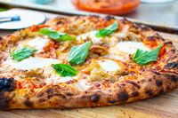 Pizza with basil leaves, cheese, and roasted toppings on a wooden board after leaving the Solo Stove Pi Prime