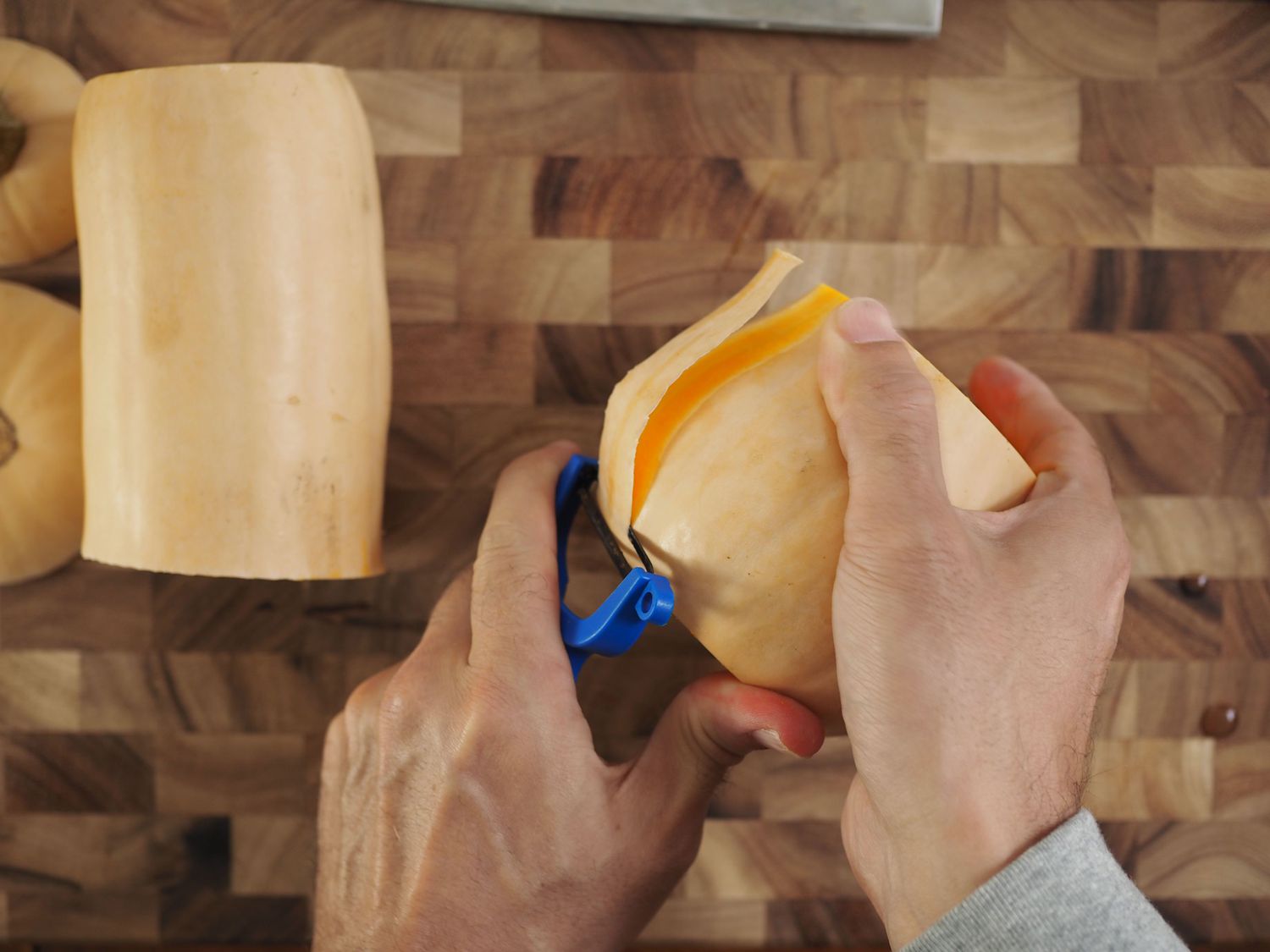 Two hands peeling a butternut squash using a Y-peeler.