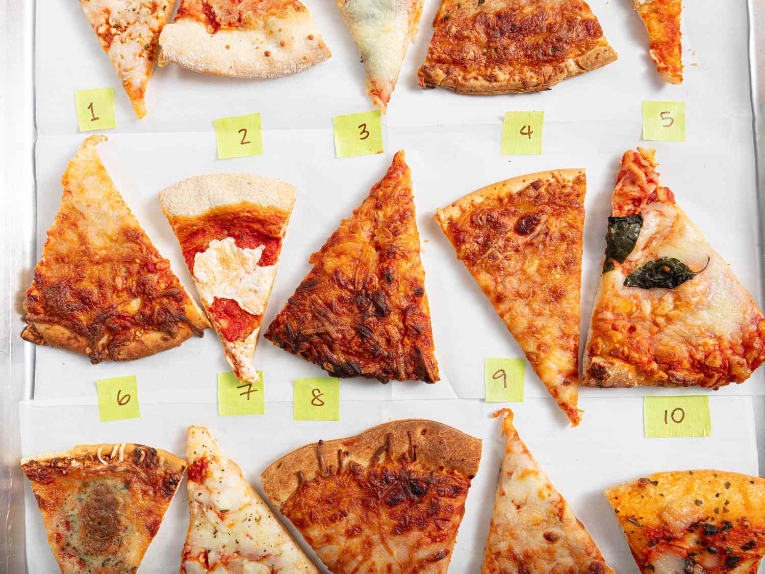 Several different types of frozen pizza on a parchment paper lined sheet pan with numbers next to them 