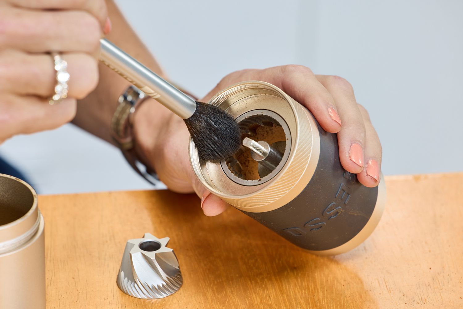 A person uses a small brush to clean the 1Zpresso J Manual Coffee Grinder