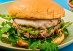 Close-up of a burger with melted cheese, slices of green peppers, cilantro, and a toasted bun on a green plate