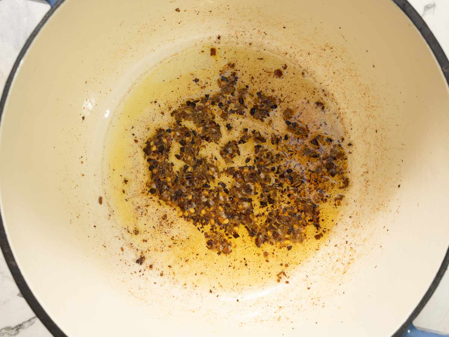 A pot with oil and fried spices in preparation for cooking