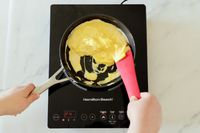 A person scrambling eggs in a small nonstick pan on an induction burner.