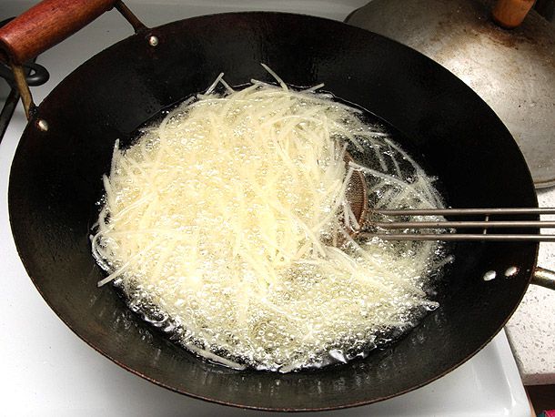 Julienned and throughly rinsed potatoes are deep-fried in a wok.