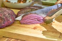 A person slices meat cooked in the Cuisinart COS-244 Vertical 36-inch Propane Smoker
