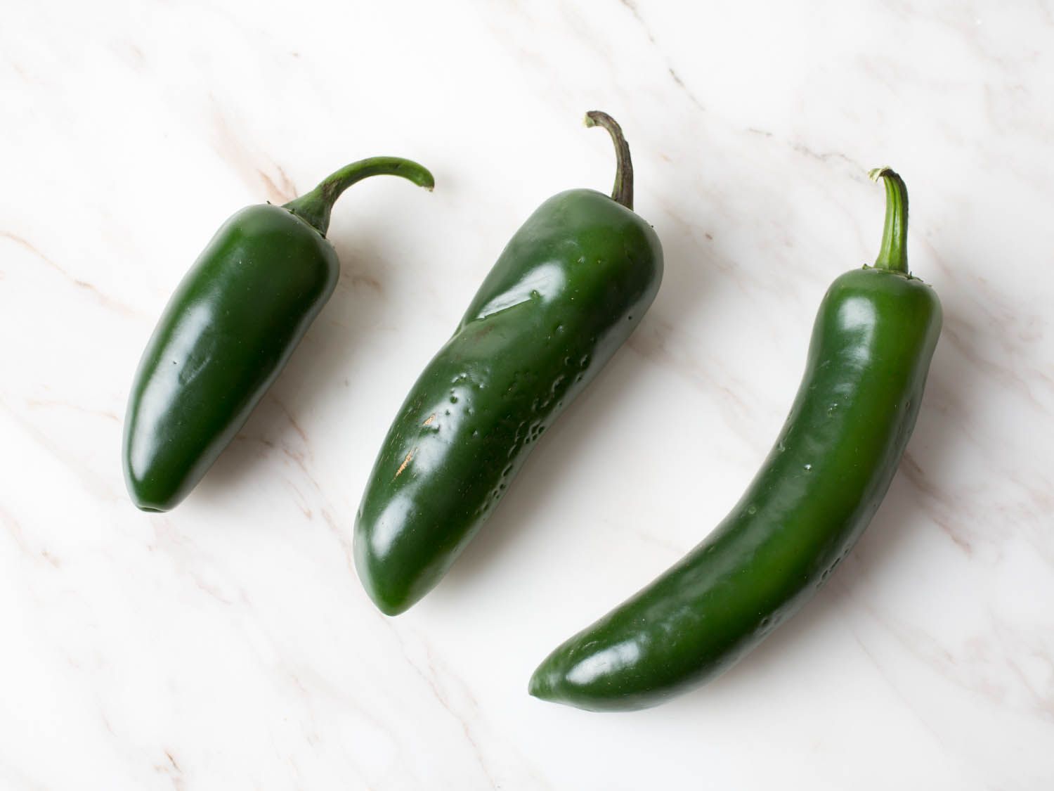 A comparison of several fresh jalapeños. One is quite small and another is long and slender.
