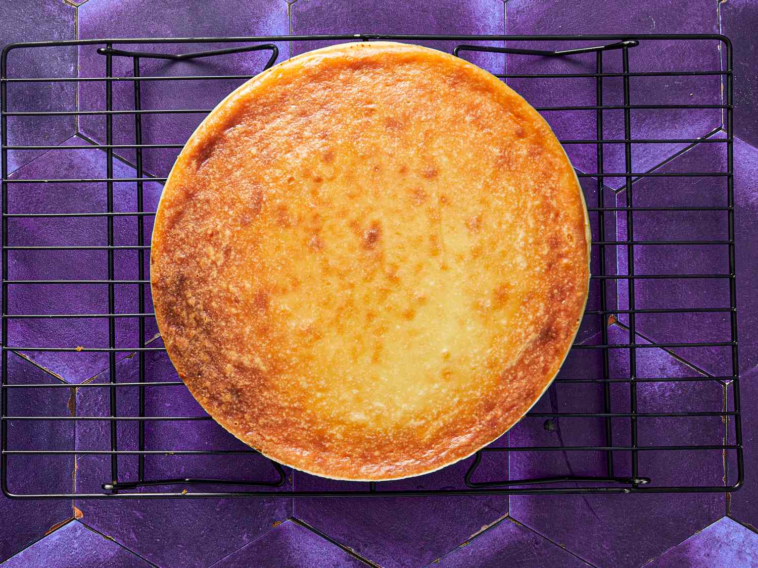 Baked cheesecake cooling on a wire rack placed on a purple surface