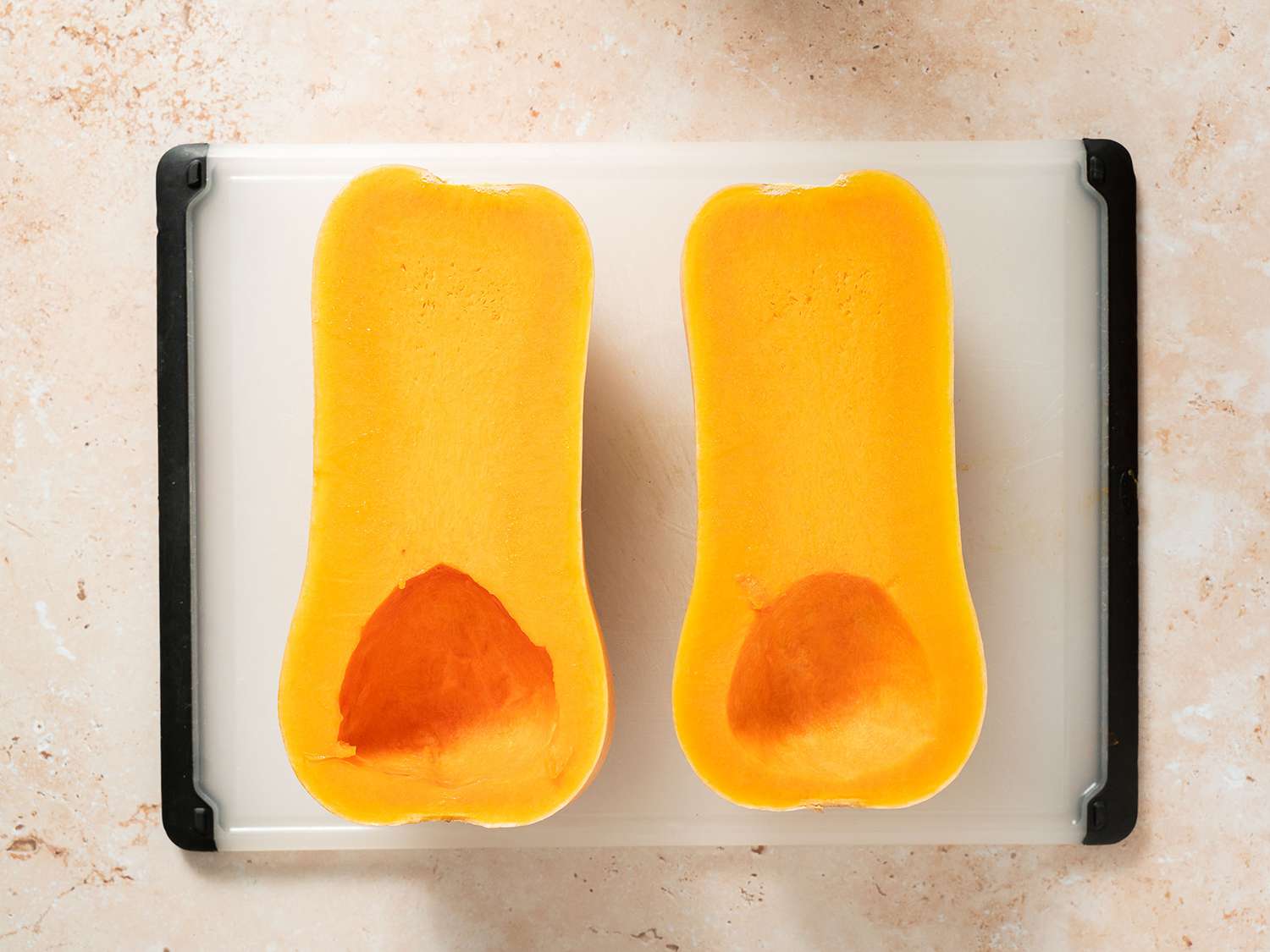 Halved and scooped out butternut squash on a cutting board.