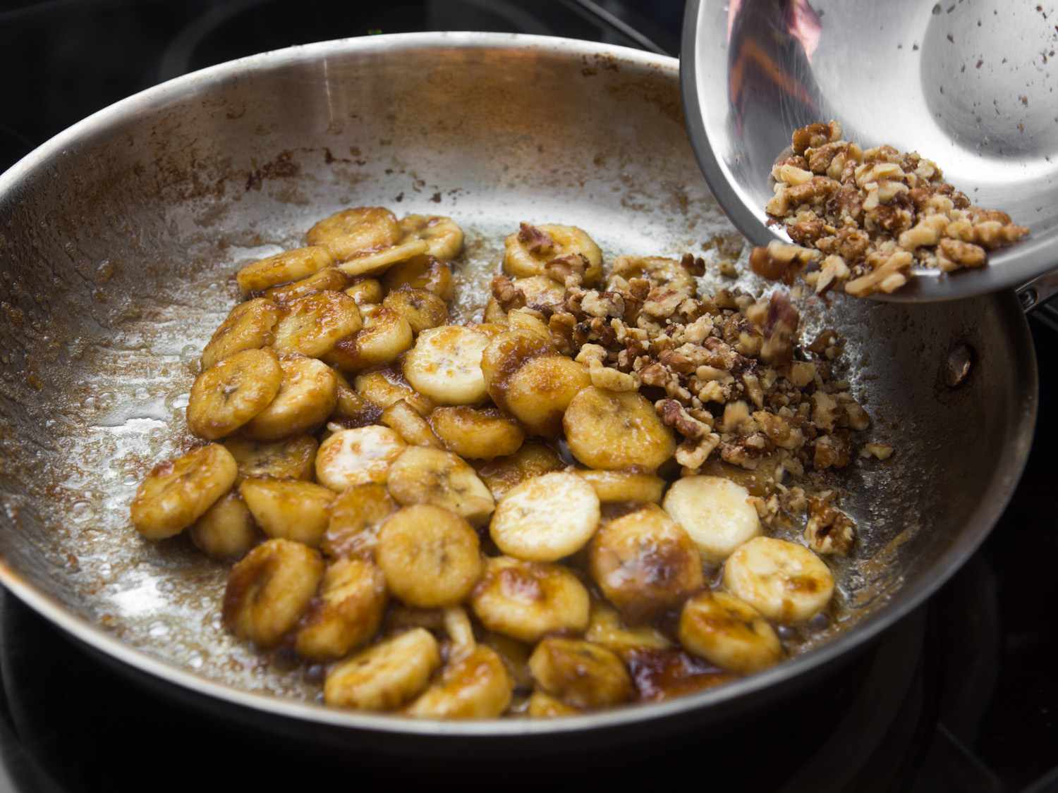 Closeup of walnuts being added to the skillet, joining the caramelized banana slices.