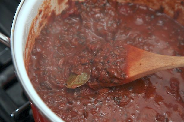 The finished vegan Bolognese sauce. A wooden spoon lifts some of the chunky, mushroom-laden sauce above the surface.