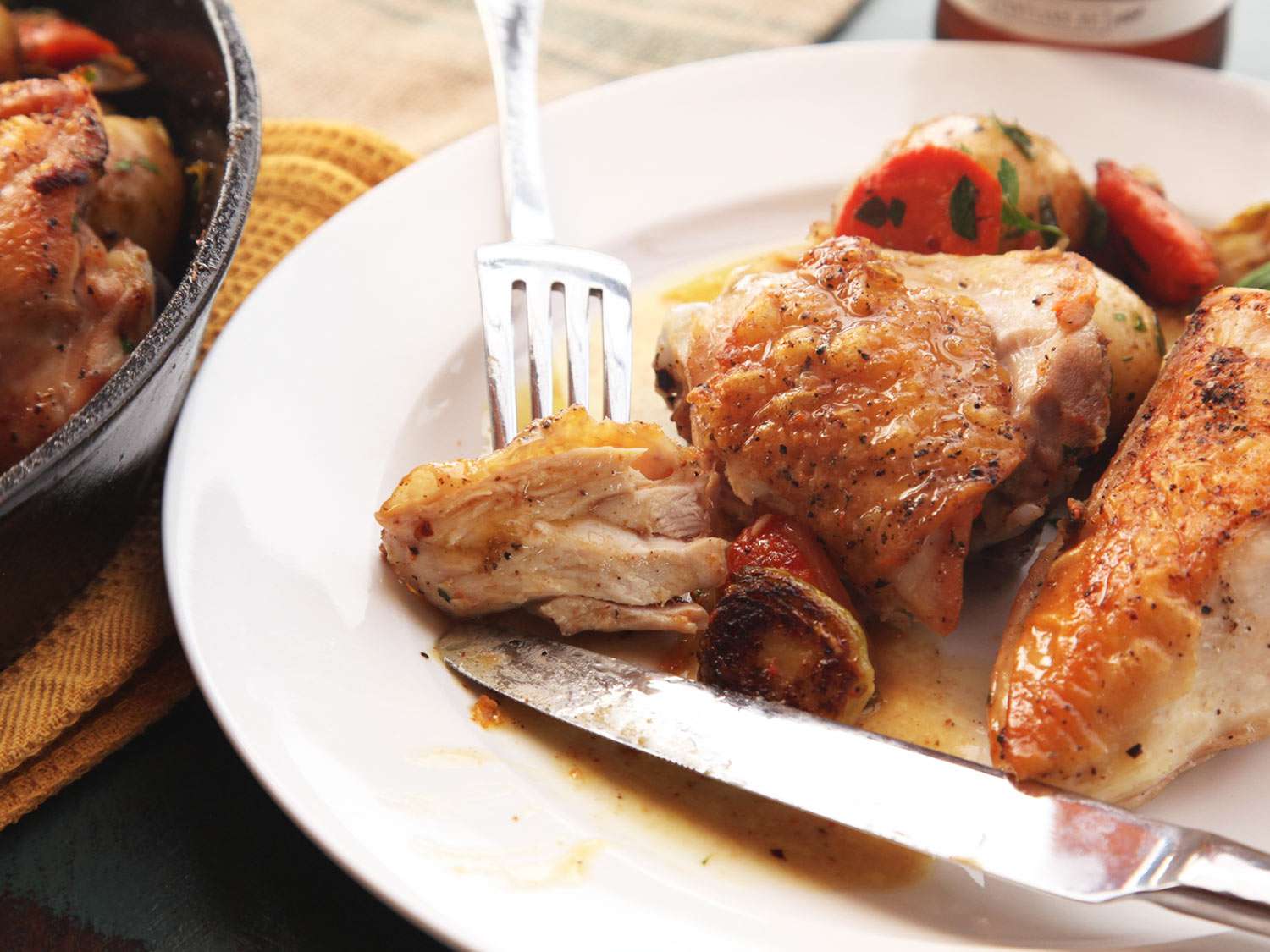 A forkful of pan-roasted chicken on a white plate with roasted vegetables