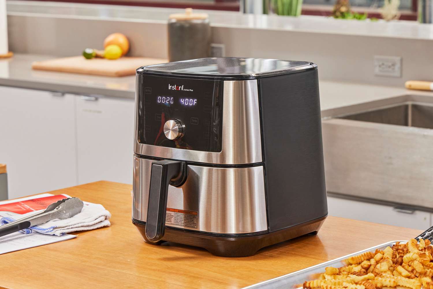 The Instant Vortex Plus 6QT XL Air Fryer on a wooden counter next to a baking sheet of fries