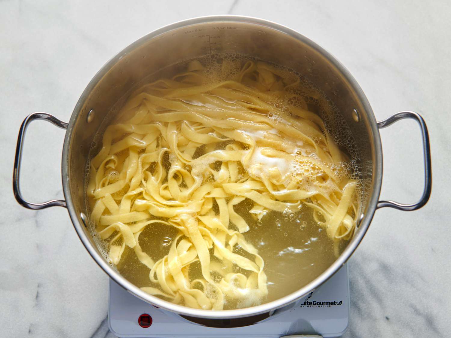 The cut gluten-free pasta being cooked in a boiling pot of water.