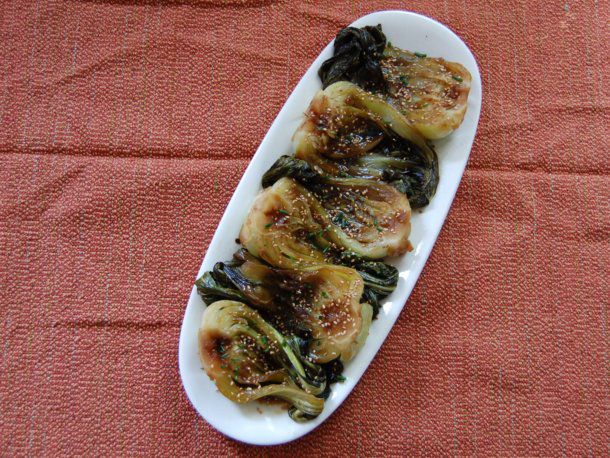 Braised baby bok choy plated on a serving dish, garnished with sesame seeds and minced chives.