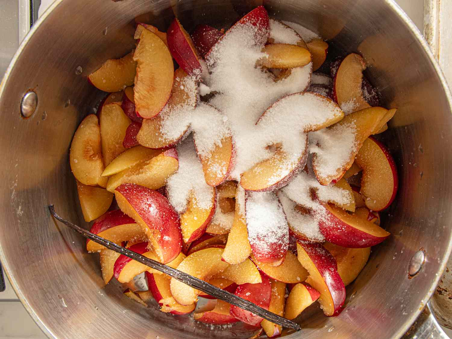 Sliced plums in a pot with sugar and a split vanilla bean