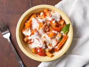 Overhead shot of bowl of baked ziti drizzled with Parmesan cream 