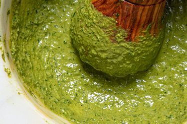 Closeup of a bowl of pesto being mixed with a wooden pestle