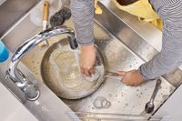 A person cleans the Tramontina 12-Inch Stainless Steel Skillet in a sink