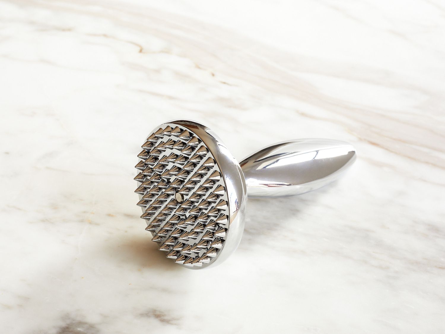 Spiked textured metal object with a handle placed on a marble surface