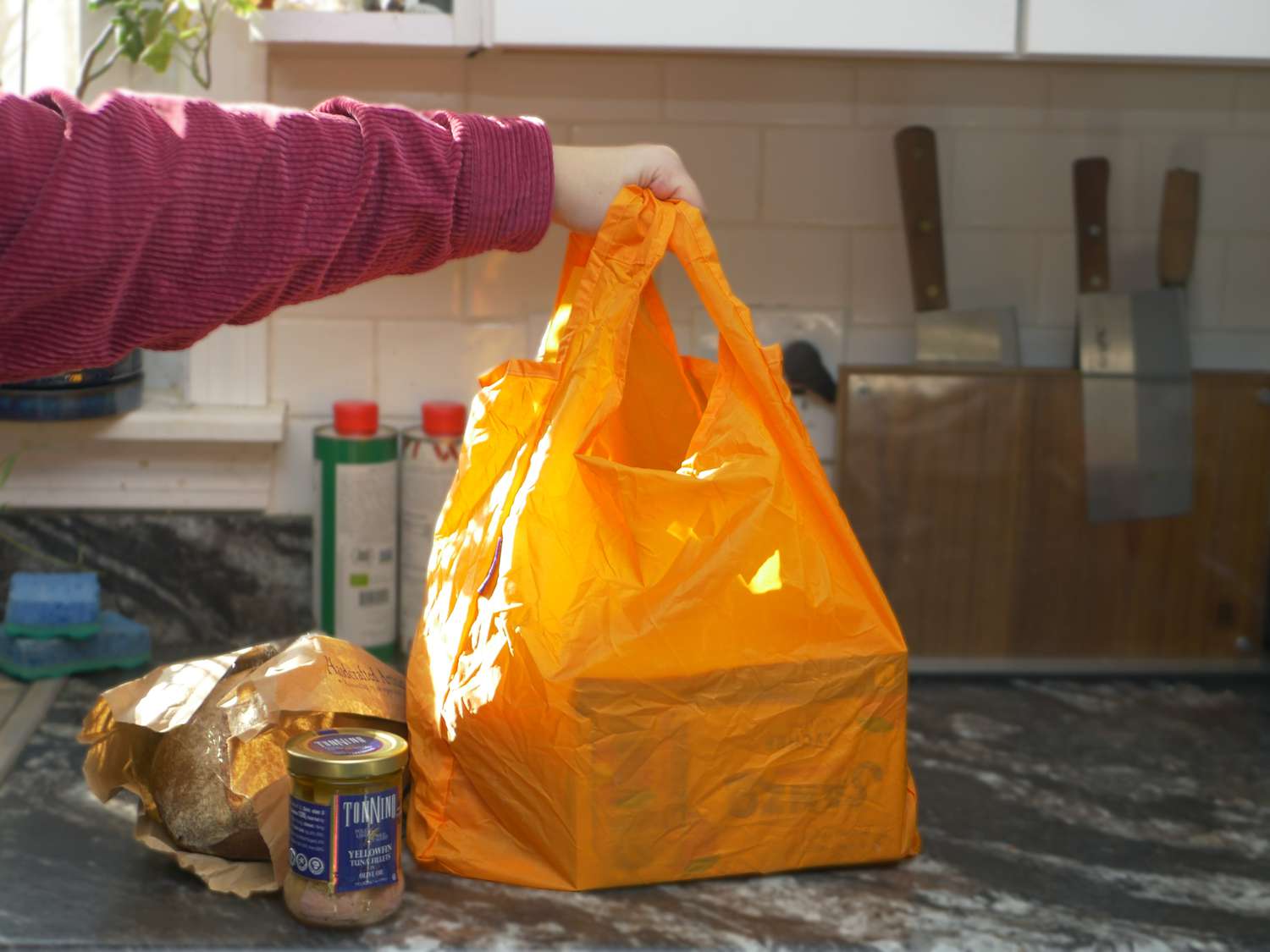 a hand holding the handles on an orange reusable grocery bag on a countertop