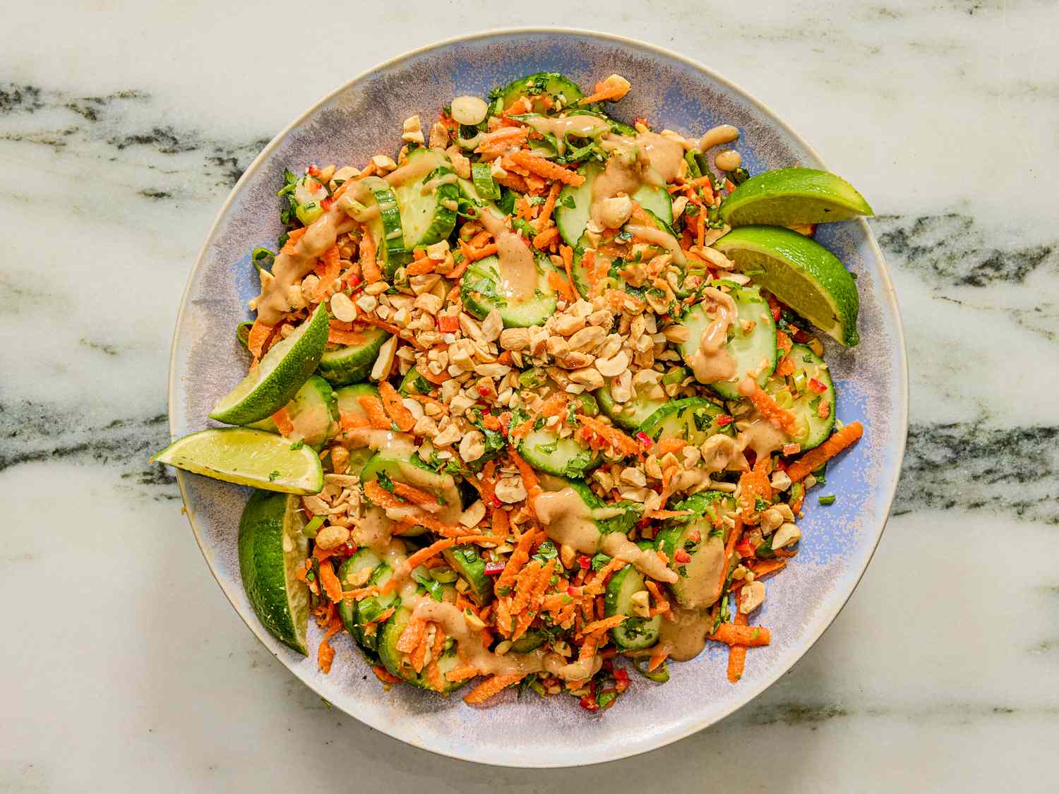 Plate of cucumber salad garnished with lime wedges and a dressing drizzle