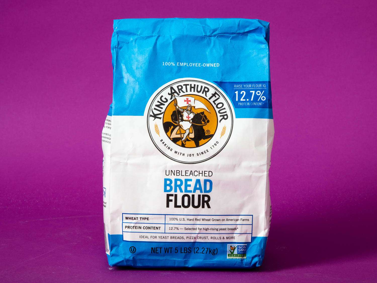 A bag of King Arthur Flour Unbleached Bread Flour against a purple background.