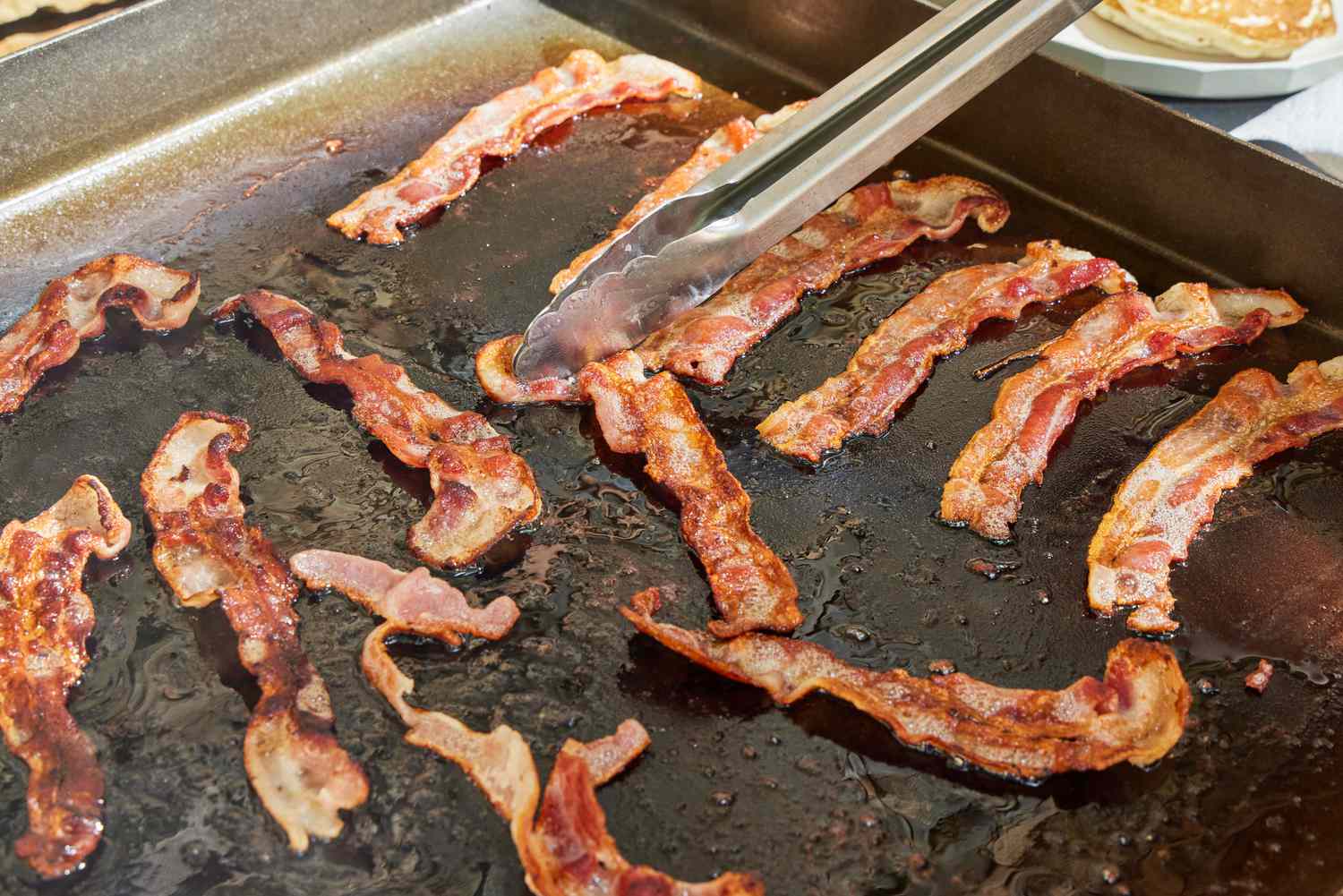 Bacon is cooked on the Blackstone 1554 Cooking 4 Burner Flat Top Gas Grill