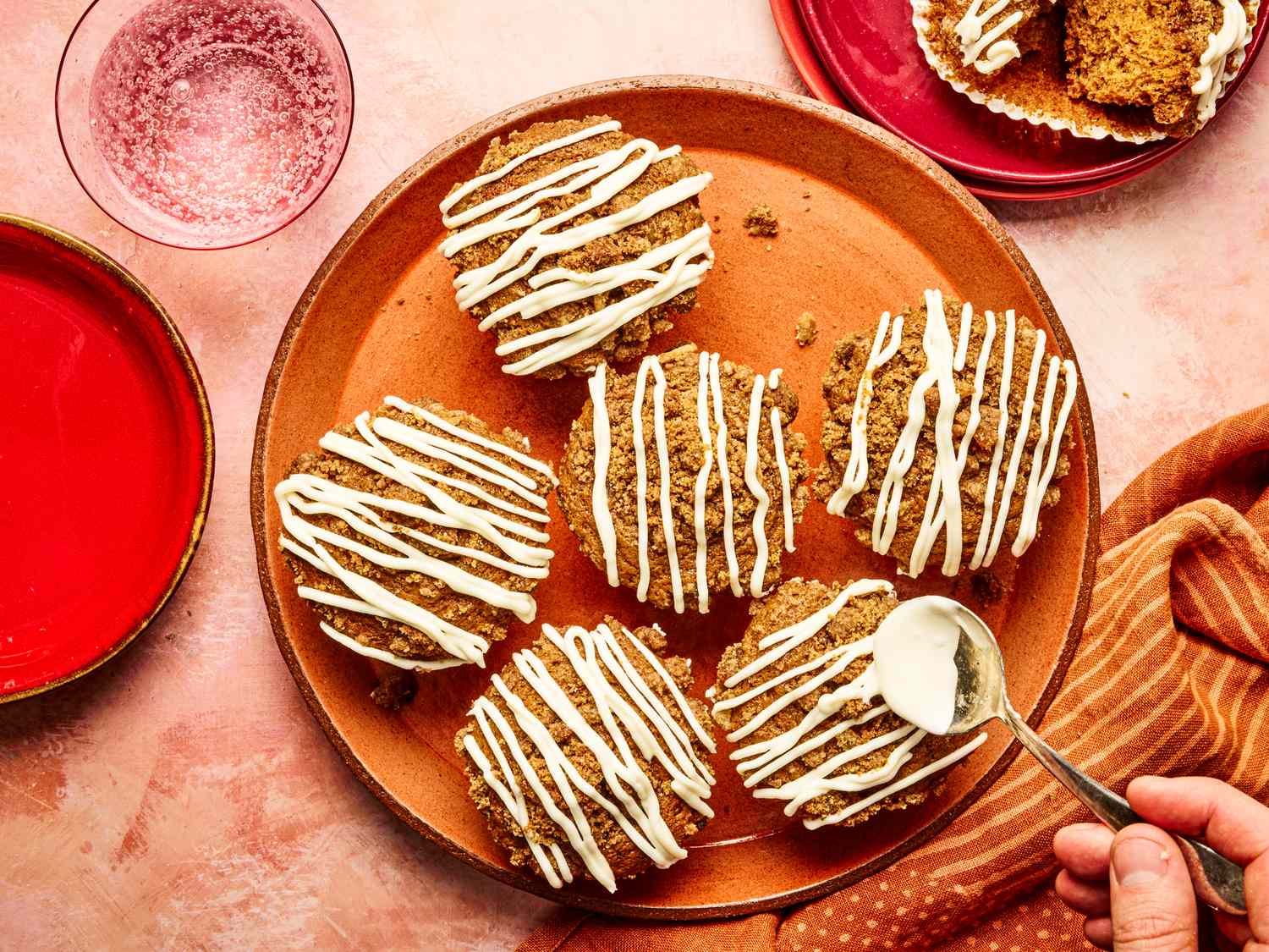 Gingerbread muffins with icing served on a plate with a hand applying more icing using a spoon
