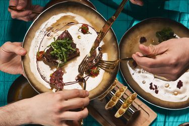Hands holding utensils and sharing plates of food at a table