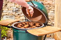 A person cooks chicken in the Big Green Egg Large Charcoal Kamado Grill and Smoker