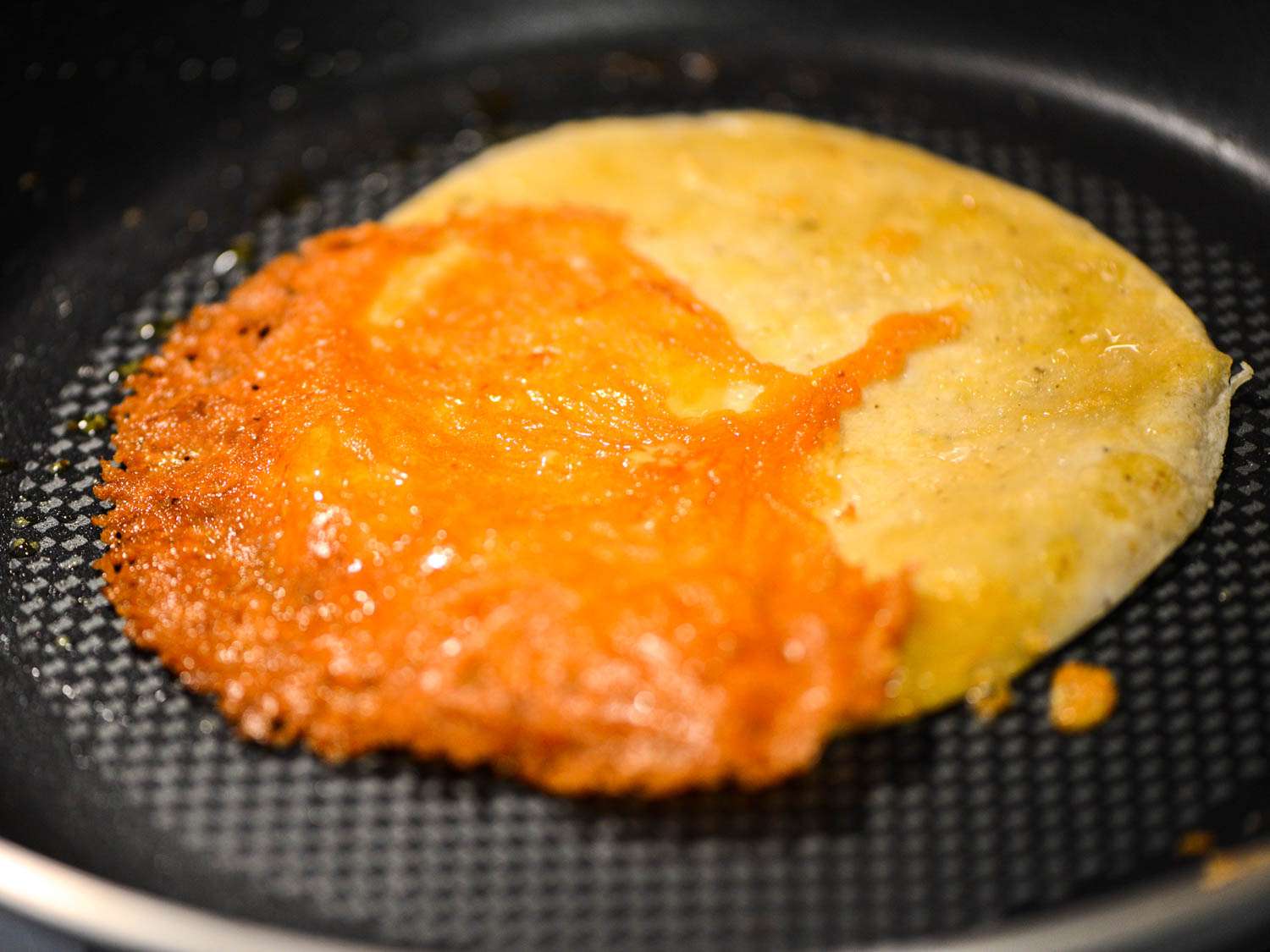 A layer of crispy cheddar overhanging on a warm tortilla in a non-stick pan