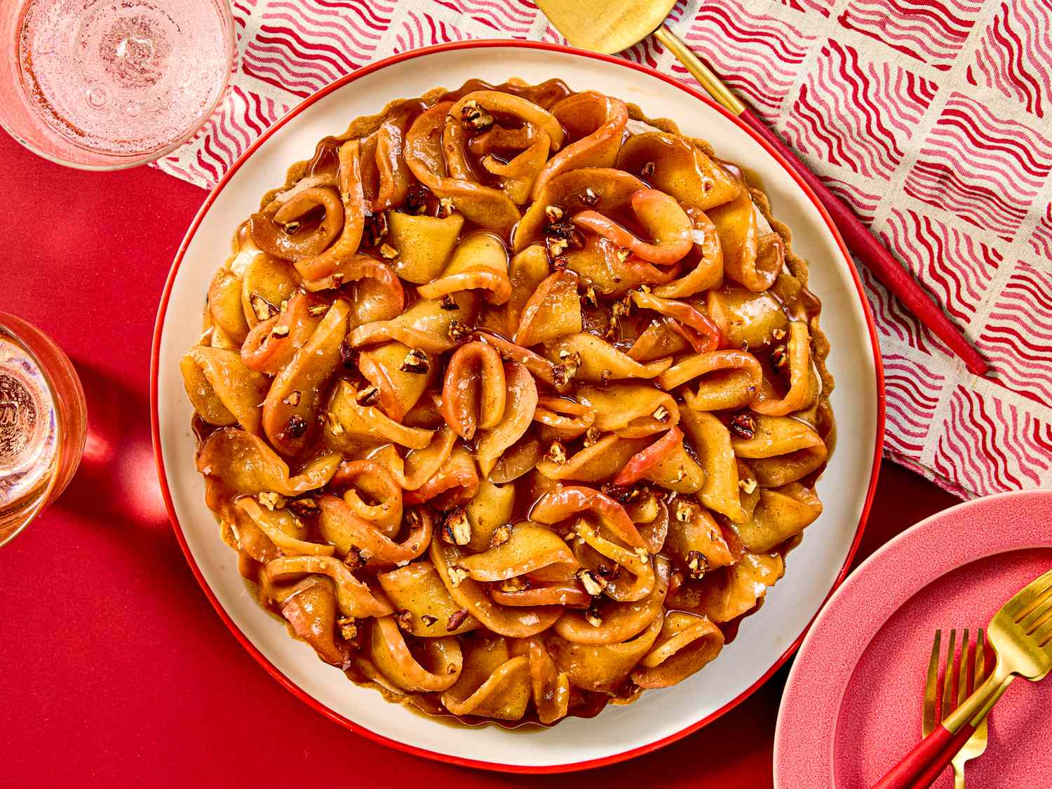 A caramel apple tart with decorative crust garnished with nuts placed on a red table setting