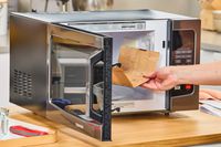 A hand placing a popcorn bag into the Toshiba EM131A5C-BS Microwave Oven