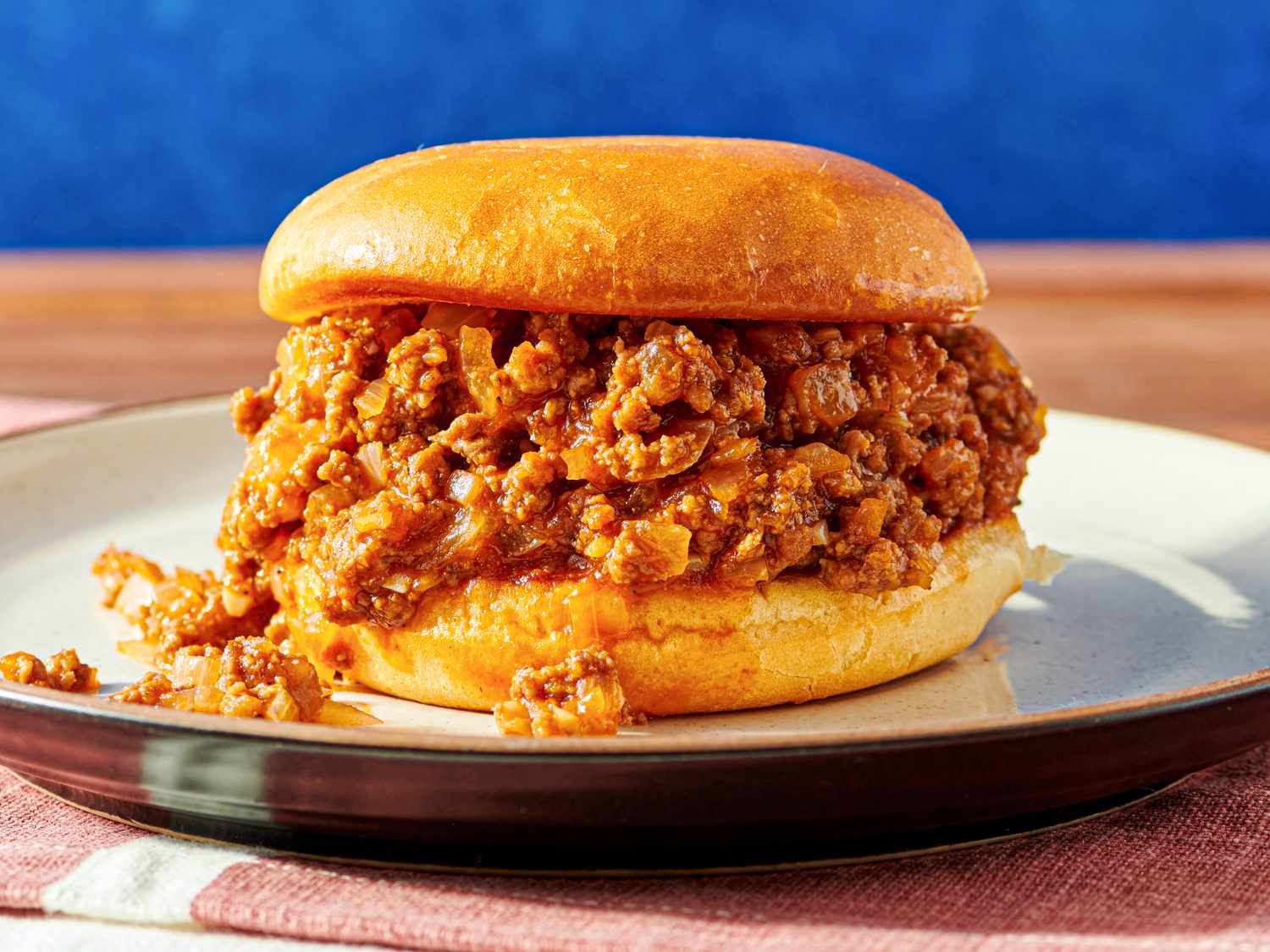 A sloppy joe sandwich on a plate featuring a bun filled with seasoned ground meat