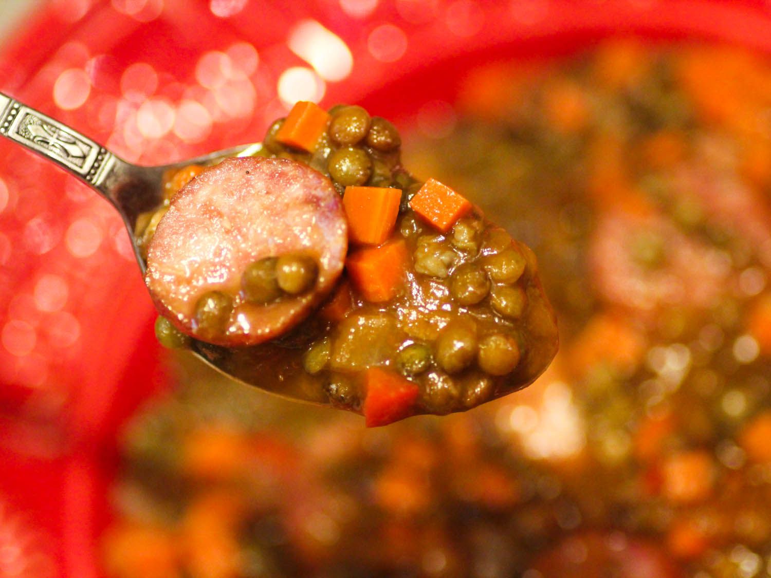 A spoonful of cotechino con lenticchie is held up to the camera.