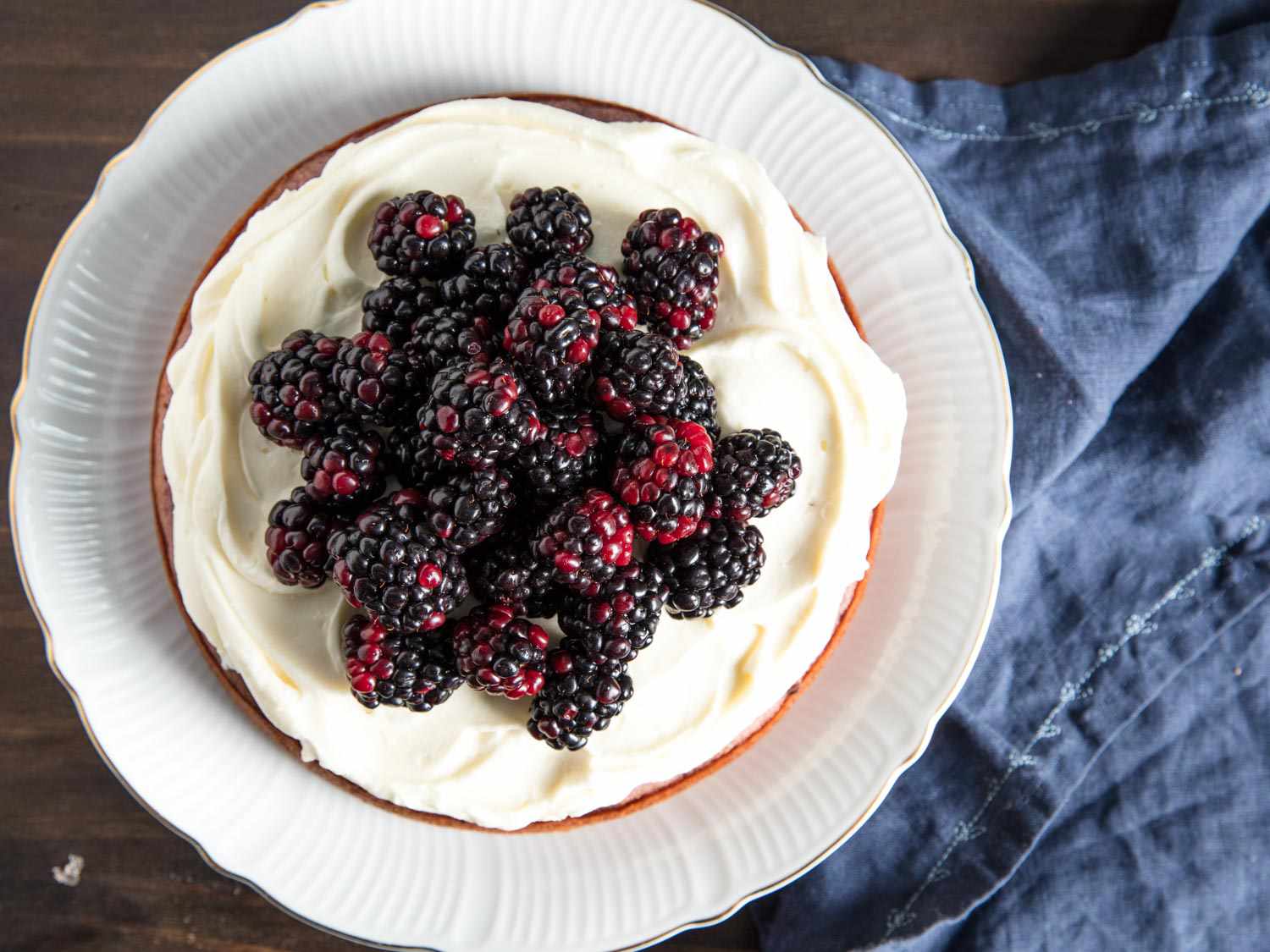 Overhead shot of finished blackberry cake on a plate, topped with cream cheese frosting and fresh whole blackberries