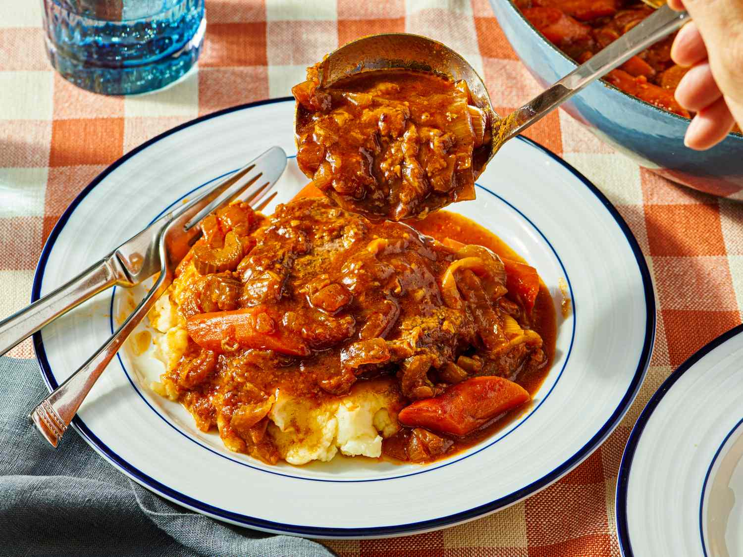 Plate of Swiss steak with mashed potatoes and a serving spoon midaction