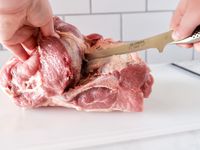 A person using the Global boning knife to cut meat.