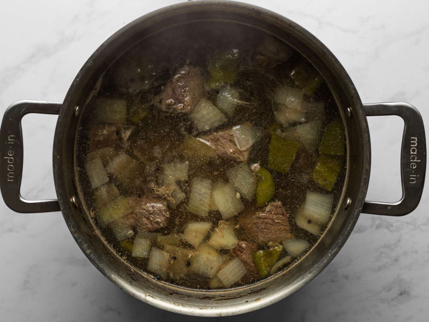 Beef, half of the bell pepper, half of the onion, salt, peppercorns, garlic, and 2 inches of water coming to a boil in a large pot over medium-high heat.