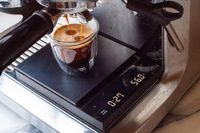 Espresso machine brewing into a glass placed on a Hario Polaris Coffee Scale displaying measurements