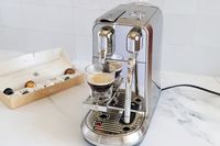 A coffee machine with a glass of coffee brewing capsules in a box next to it