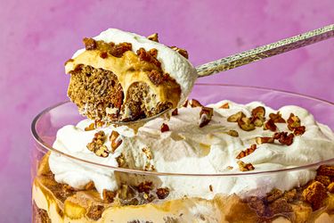 Banana bread trifle with whipped cream and pecans in a glass bowl spoon scooping a portion