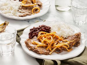 Plate with steak, cooked onions, rice, and beans on a table setting